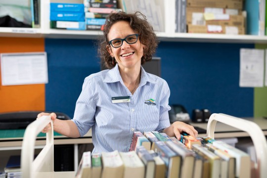 Smiling librarian from Moreton Bay Region Library holding onto a book trolley.