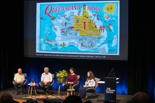 Four people sitting on stage with a large projection of a tea towel behind them.