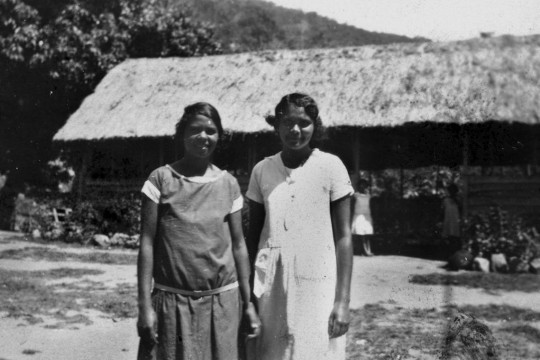 Two Aboriginal girls in front of a grass hut