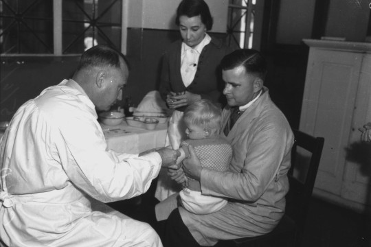 A black and white photograph of Dr. Weaver immunising a child while a nurse looks on, Brisbane, 1941