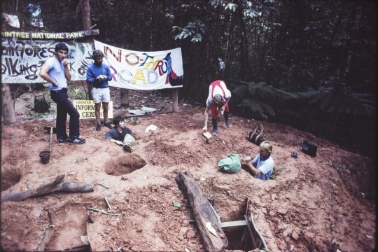 Two buried protestors and three other protestors standing around during the Daintree Road blockade, August 1984.