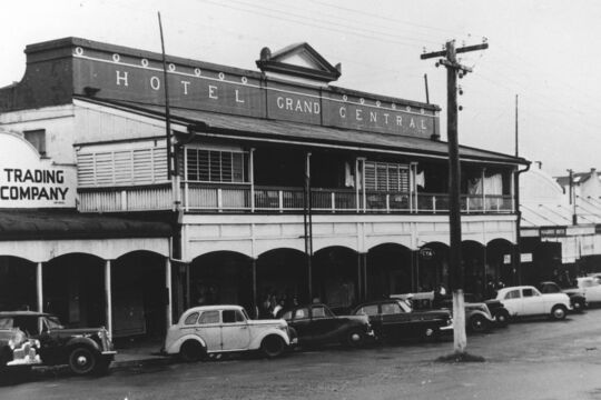 Black-and-white photograph of the Grand Central Hotel, a two-storey timber building with a balcony and arched verandah, with several mid-20th-century cars parked along the street in front.