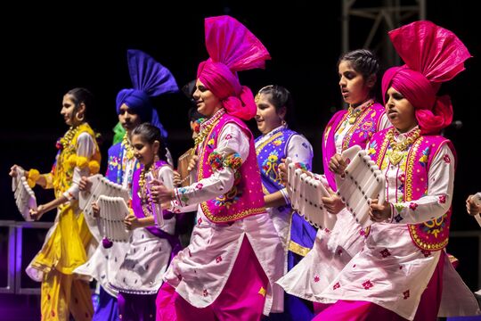 Group of people dressed in colourful clothing, doing Bhangra folk dancing