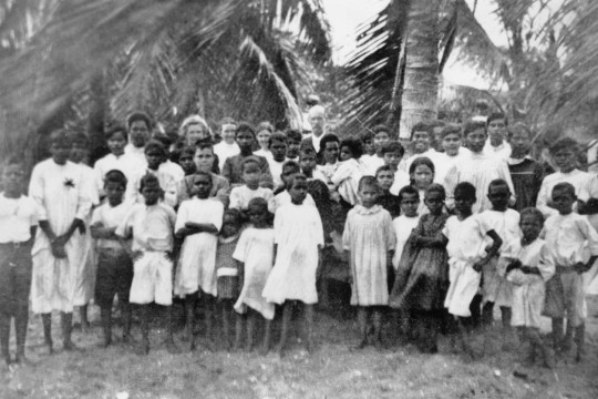 A group of Aboriginal school children standing in front of palm trees
