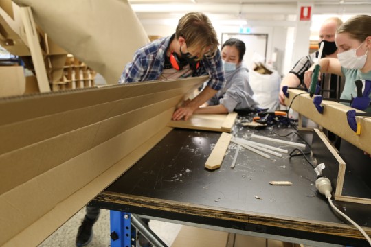 Students folding long pieces of cardboard into beams.
