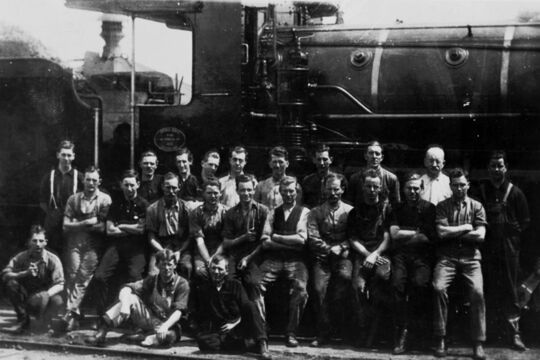 Group of men standing beside a steam engine train