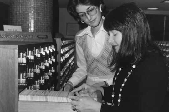 Black and white photograph of two women flicking through the card catalogue at the State Library.