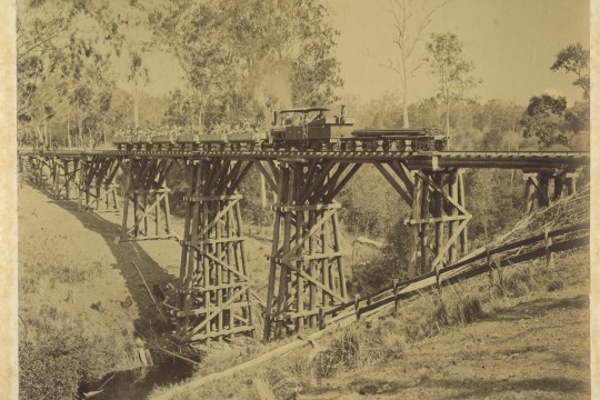 View of an early locomotive crossing a deep creek ravine via a wooden structure
