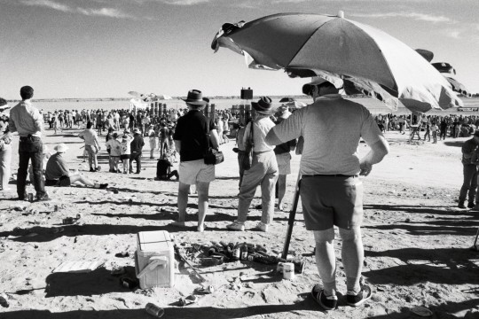 Man with an esky standing under an umbrella at the race track during the Birdsville races, Queensland, 1990