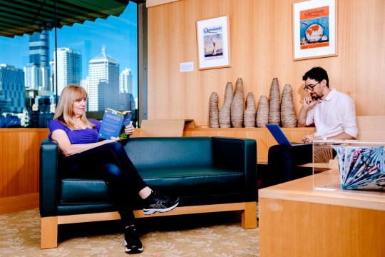 Two people sitting inside at the library. One person is reading a book and another is using a laptop.