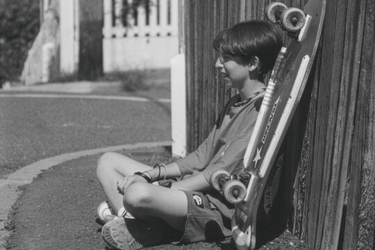 Boy sitting on the side of the street with his skateboard.