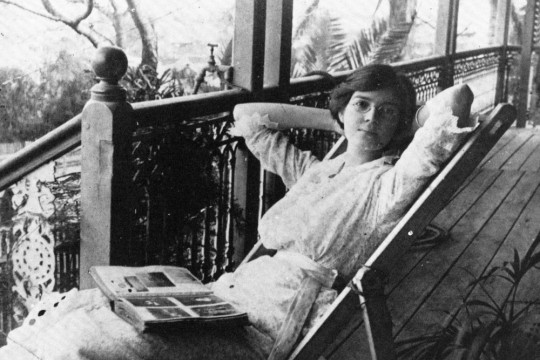 A woman sitting on a verandah with a book open on her lap