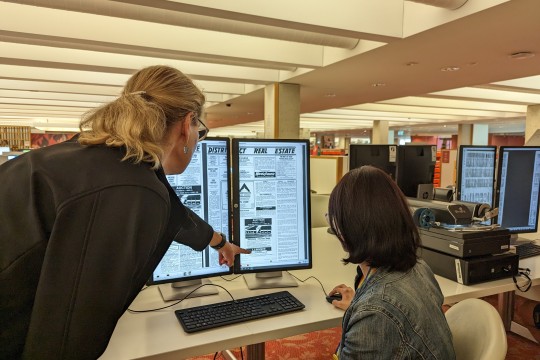 staff member showing client how to use microfilm reader in library
