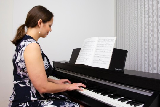 Woman sitting at a piano with her hands pressing the keys.