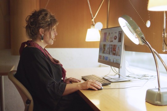 Woman sitting at a computer with desk lamp. 