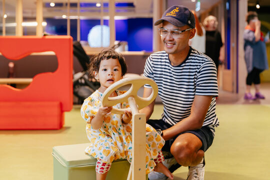 Father and child playing with a toy steering wheel.