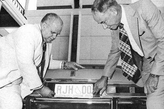 Photograph of Russ Hinze affixing his personalised plate to a car