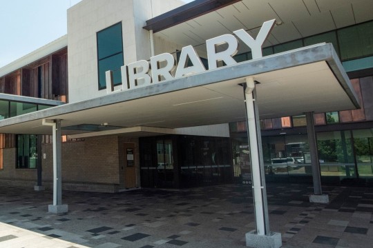 A blue sky, front of a modern with a library sign
