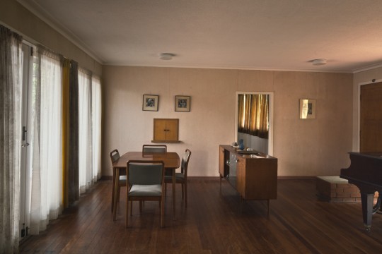a sparse room with mid century table and chairs next to a window with curtains 