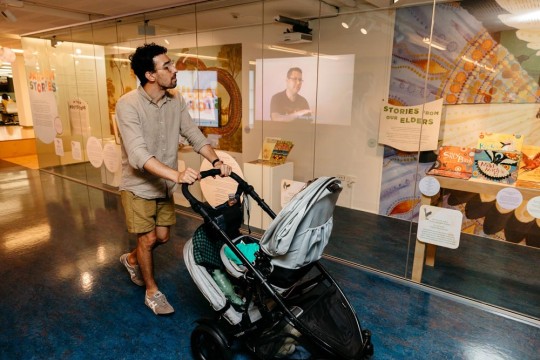 Man will child in stroller exploring the Jarjum Stories showcase at State Library.