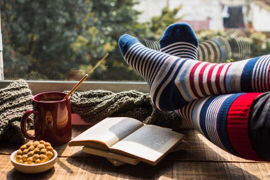 Wintery home looking out of window, books, hot drink, stripey socked feet