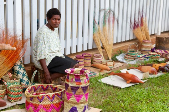 Papua New Guinea trader selling colourful woven baskets, and animals carved out of wood