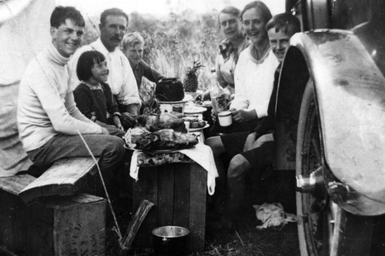 Family group of two adults and 5 children eating lunch beside a truck, 1918