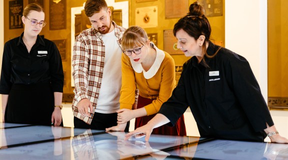 A male and female guest exploring the digital screens in the World War II Gallery at Anzac Square with guidance from staff