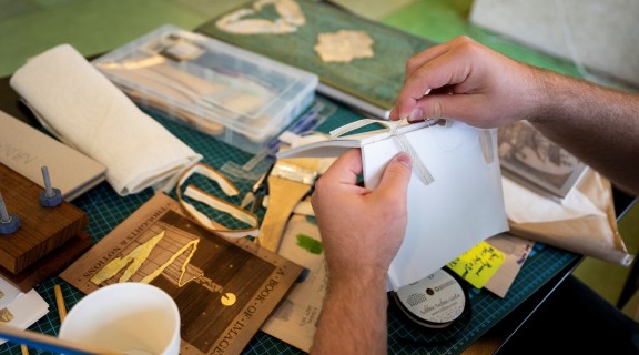 hands work on book binding with materials in the background