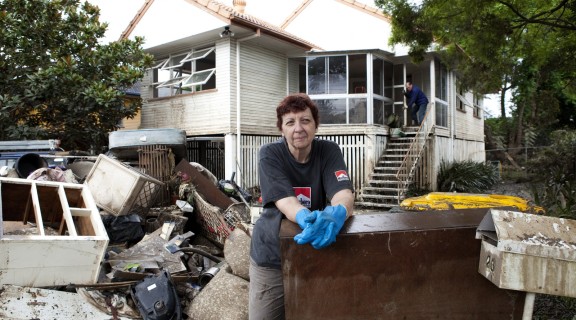 a person stands in front of her flooded home in Fairfield, debris is in the foreground 