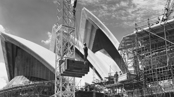 Black and white photograph from 1971, showing construction of Sydney Opera House, including a crane with the Hornibrook logo in the foreground.