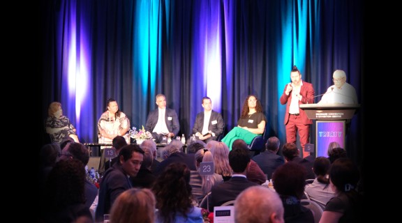 A panel of people sitting on stage while an audience watches them.