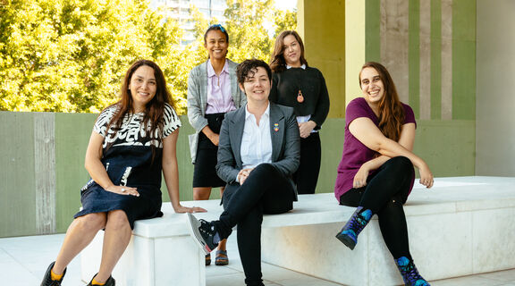 Five people sitting at State Library together. They are sitting on the QLDTerrace and are all smiling.