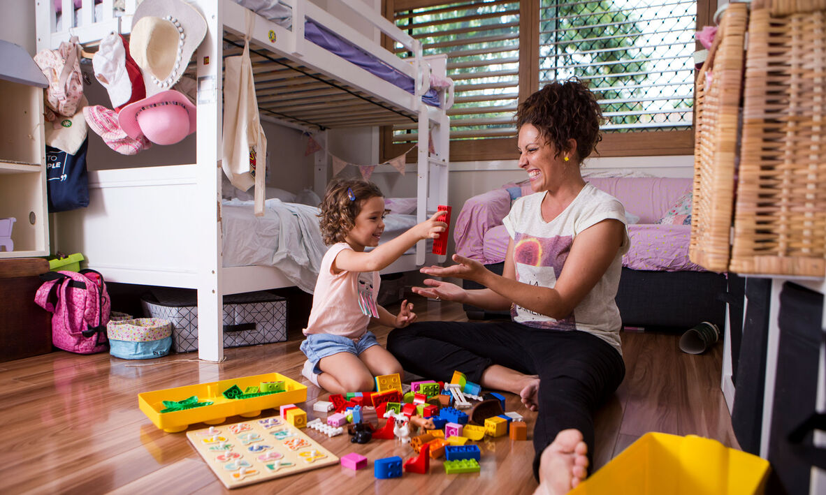 Mother and child playing with blocks on the floor of a bedroom.
