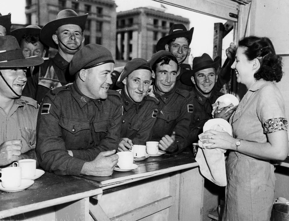 Several Soldiers enjoying a cup of tea, leaning on a bench, at the Silver Hut, Brisbane, ca. 1942.