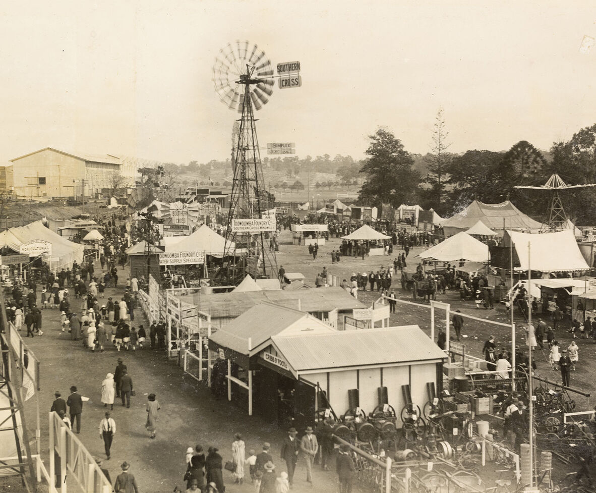 Old photograph with sheds, a windmill and crowds walking. 