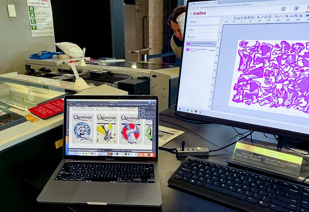 A laptop shows front covers of the Queensland magazine, and another computer display shows a purple printing file that is being engraved on the laser cutter in the background of the image