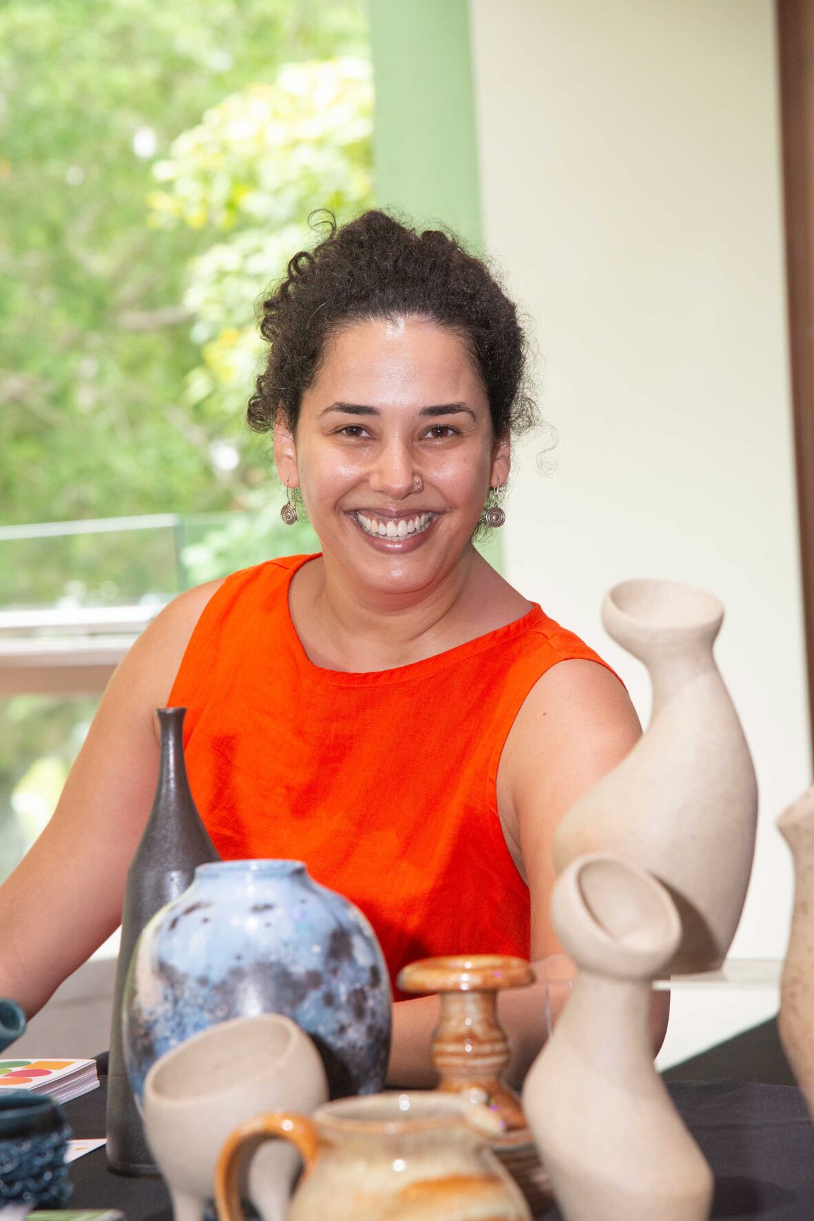 Woman wearing orange at table of ceramic sculptures
