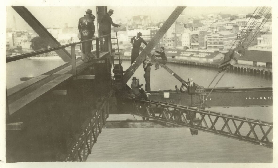 Sepia toned photo taken from the steel support beams of the Storey Bridge, picturing riggers high above the Brisbane River