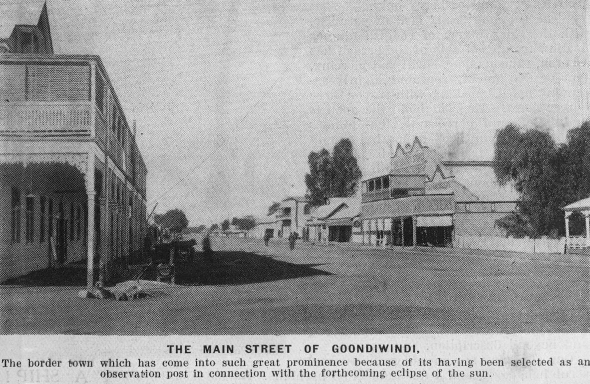 A vintage black-and-white photo of Goondiwindi's main street, featuring wide roads, wooden buildings, and sparse trees. The street appears quiet, with few people. Photo caption reads: "THE MAIN STREET OF GOONDIWINDI. The border town which has come into such great prominence because of its having been selected as an observation post in connection with the forthcoming eclipse of the sun."