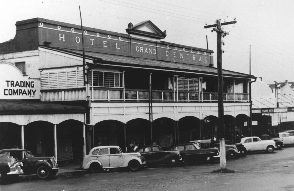 Black-and-white photo of the Grand Central Hotel with a verandah, vintage cars parked along the street, and shopfronts nearby.