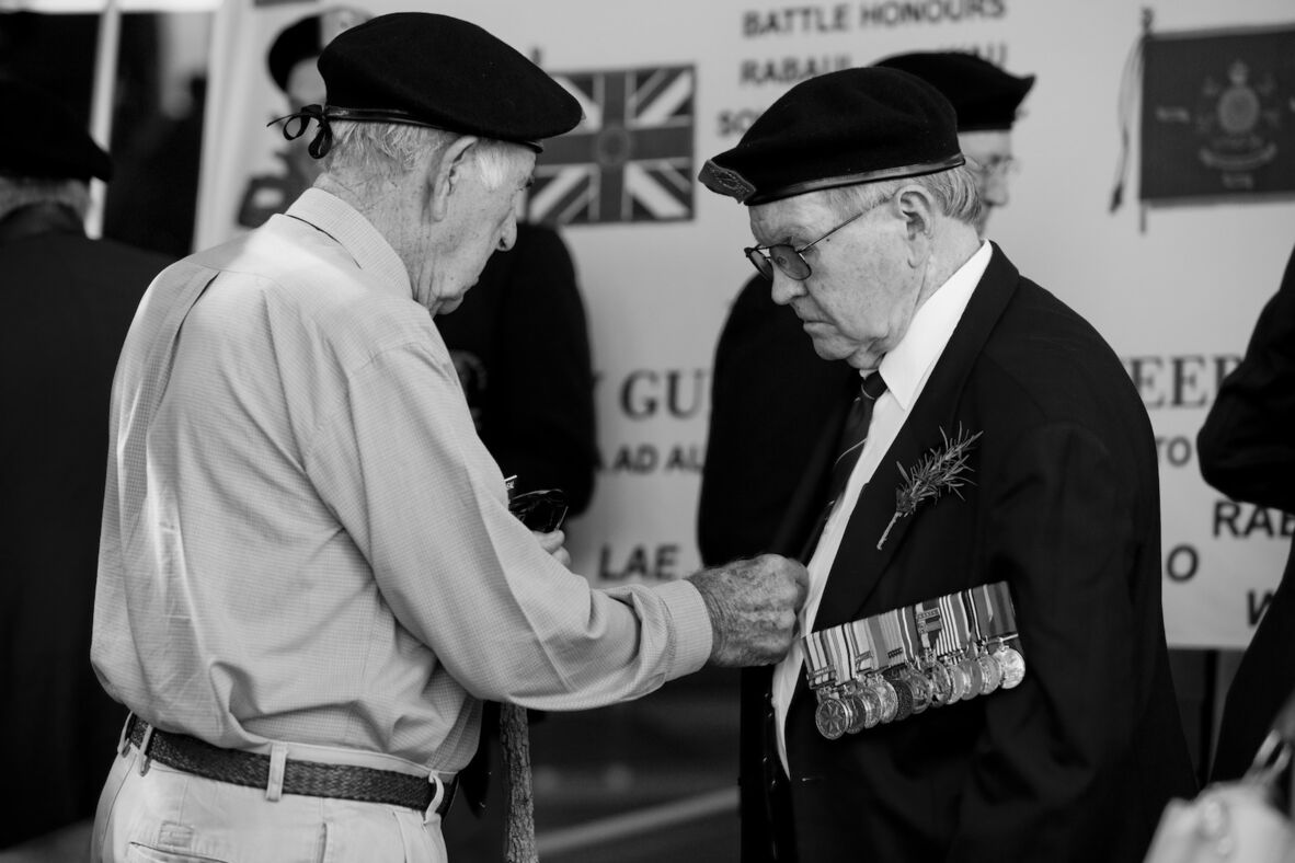War veteran reaching out to another veteran wearing military medals and a sprig of rosemary at the Brisbane Anzac Day Parade