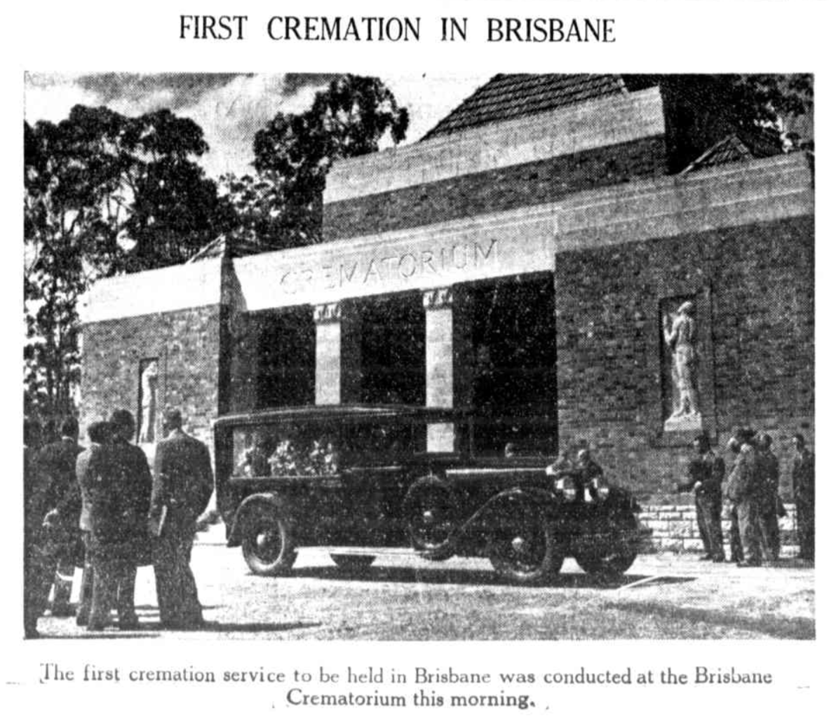 Black and white historical photo of Brisbane's first cremation. People stand by a hearse outside a brick crematorium with trees in the background.