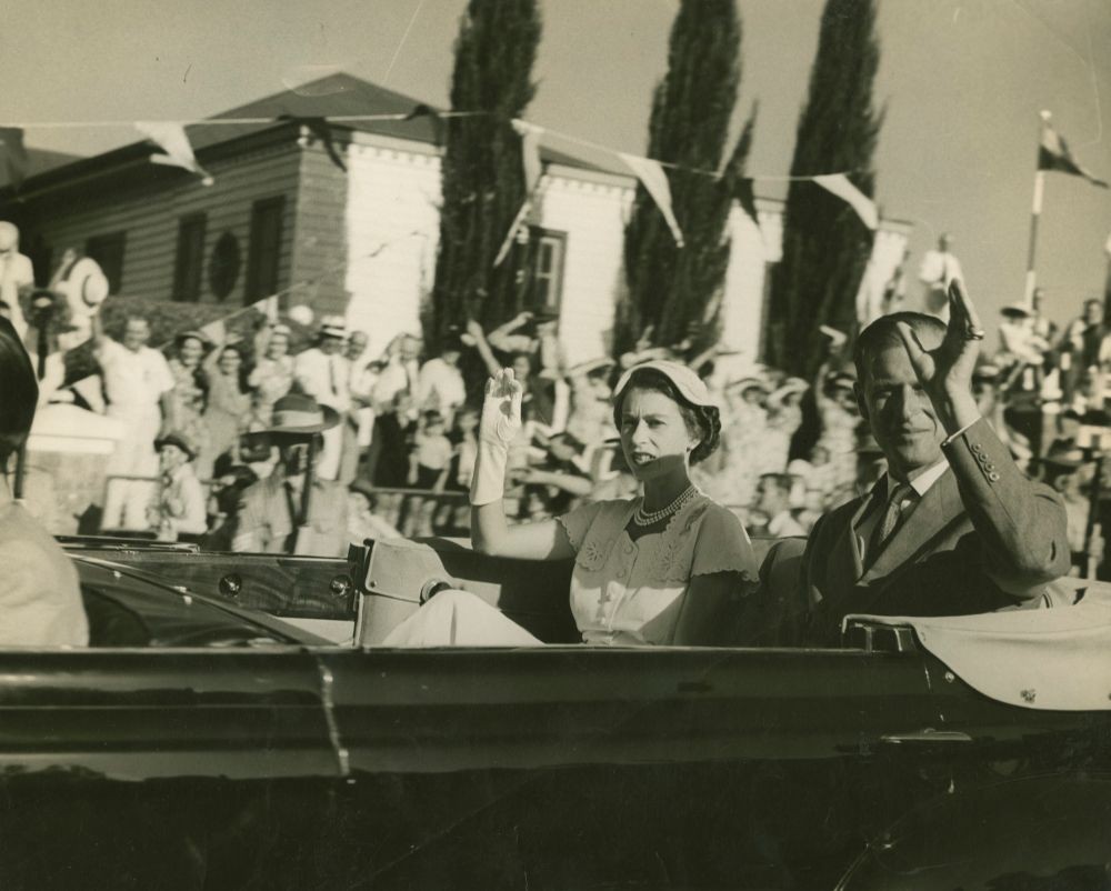 Queen Elizabeth ll and Prince Philip seated in back of car waving to crowds, Bundaberg, Queensland, 1954