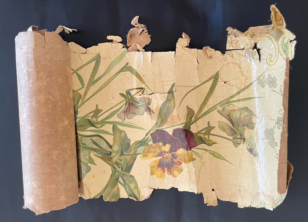 Torn, rolled piece of vintage floral wallpaper, heavily cracked and damaged.