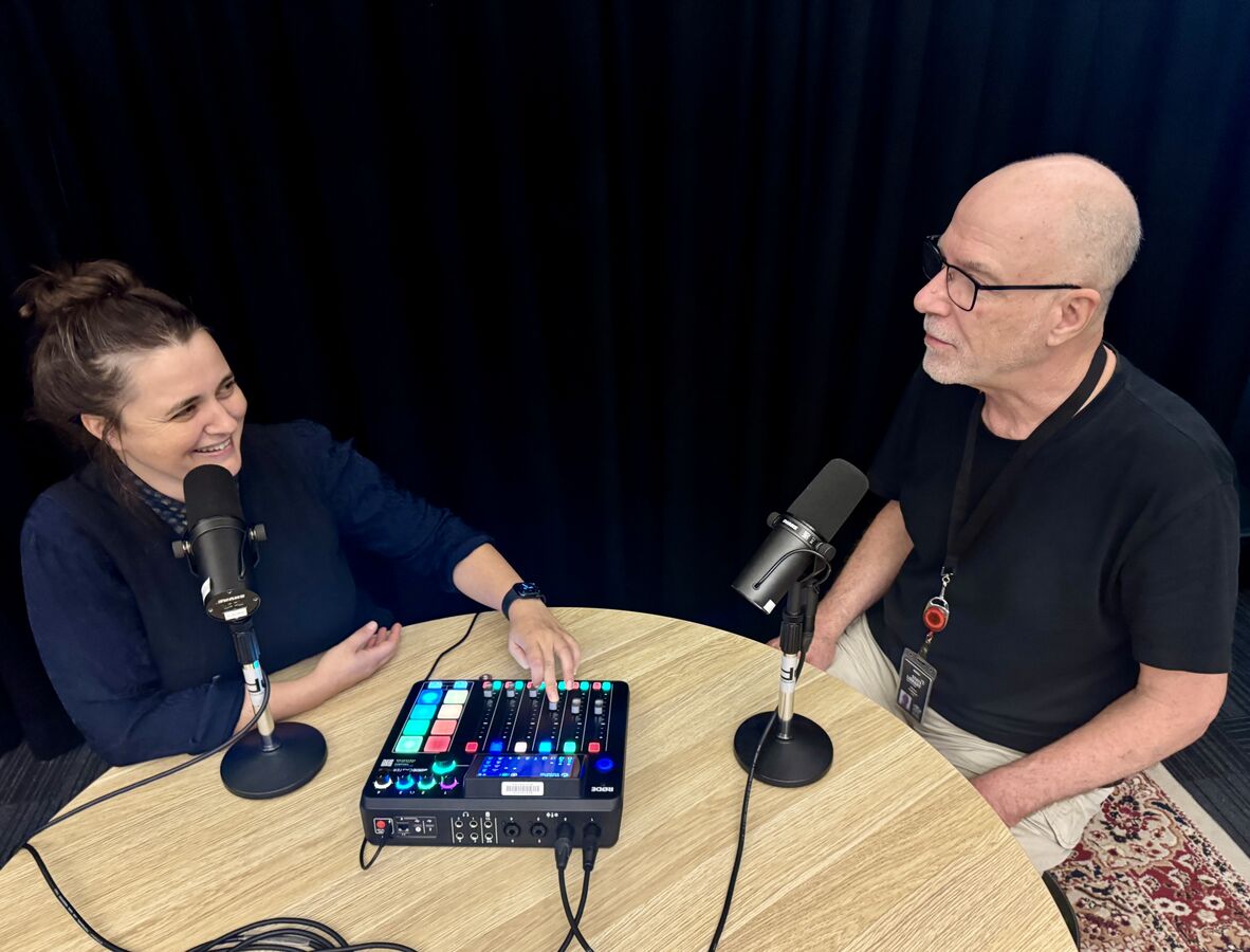 A photo of two people sitting at a round table with podcasting equipment.