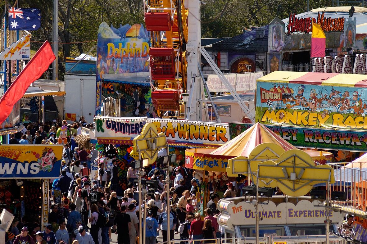 Colourful photo showing a crowd moving through the show in 2004, including rides and stalls in bright colours