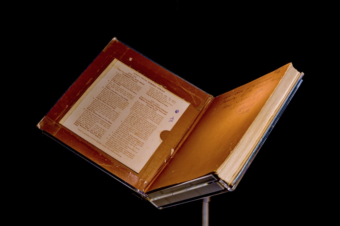 Old, open book with an inscription in the front cover on display on a stand.