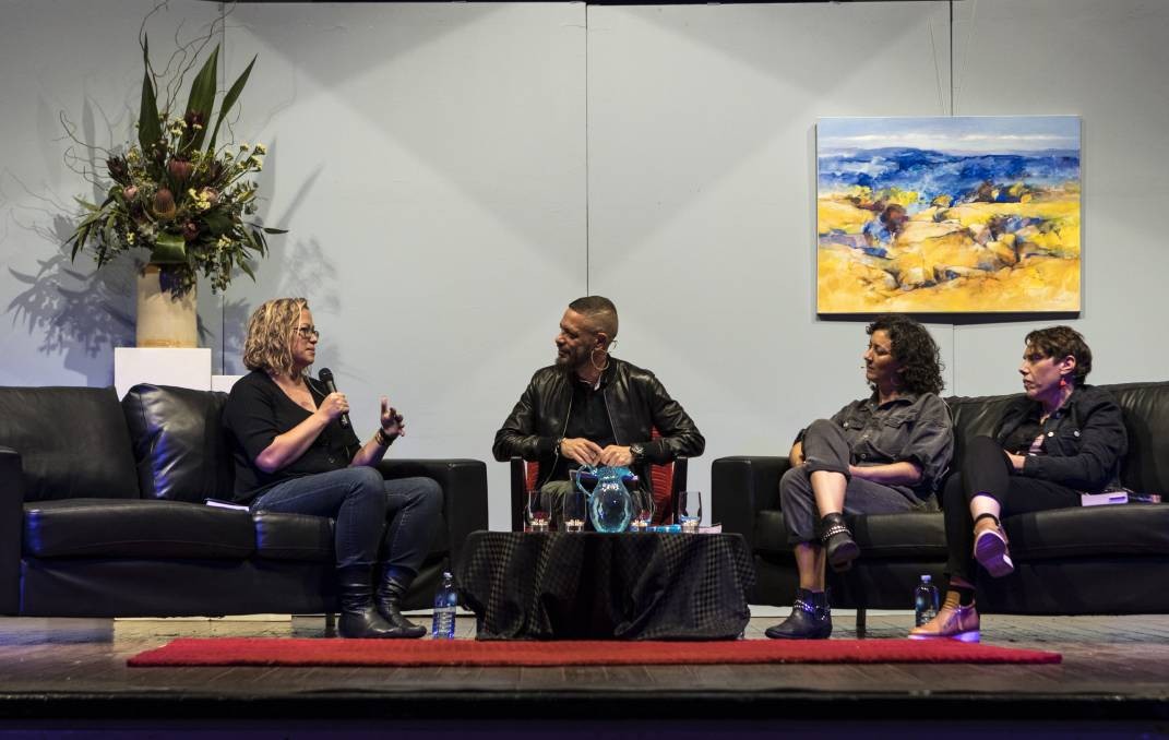 A view of a theatre stage, mid-writers festival panel with a painting and flowers in the background. Lisa Fuller, Daniel Browning, Mykaela Saunders and Nardi Simpson sit on couches.