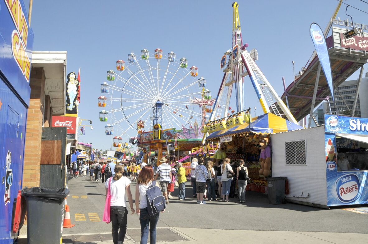 colourful image showing a ferris wheel and sideshow alley at the Ekka in 2009, against the backdrop of a blue sky